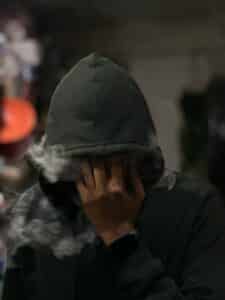 Man with hood over face blowing out smoke