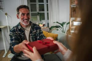 Smiling man receiving a red gift box from another person at home
